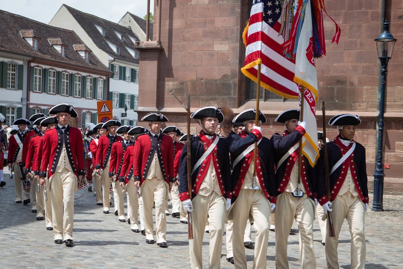 Army music unit wearing 18th-century style uniforms participates in parade.